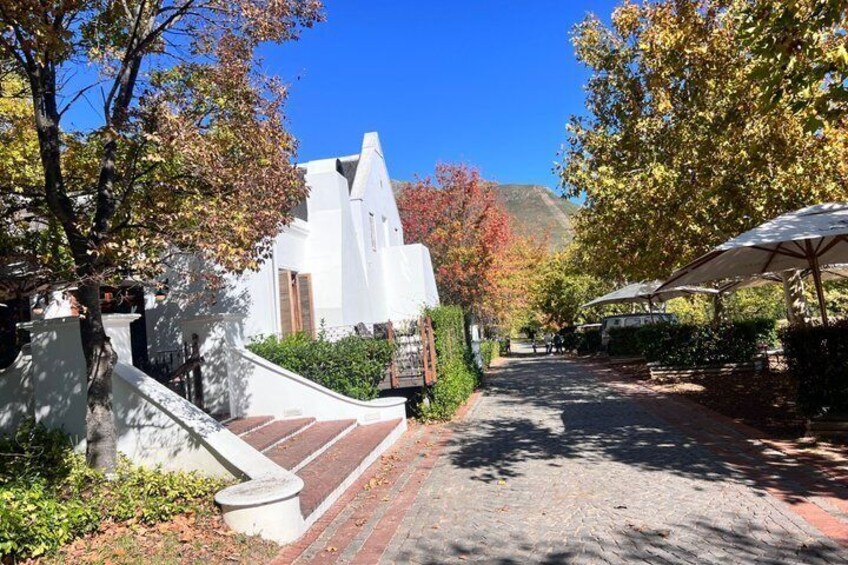 A white building with a sloped roof, a paved pathway, and trees with autumn foliage. 4