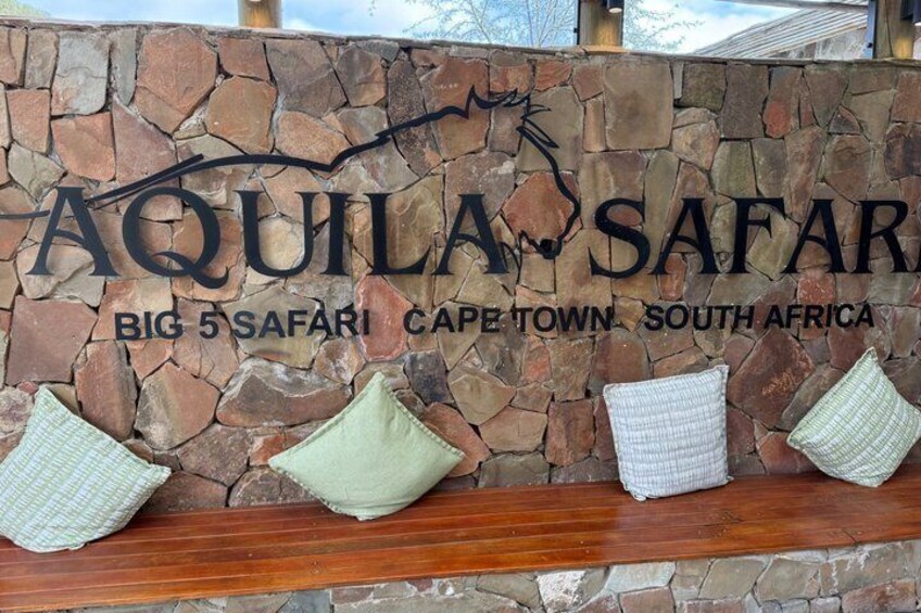A stone wall with 'AQUILA SAFARI' signage and a bench with cushions. 2