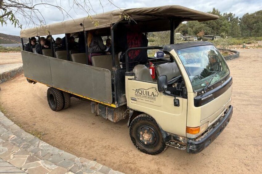 A beige off-road vehicle with 'AQUILA' branding parked on a dirt surface. 4