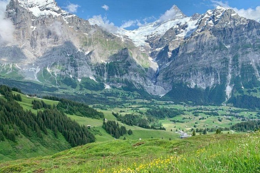 Een bergachtig landschap met besneeuwde toppen, een vallei met groene velden en een heldere lucht. 5