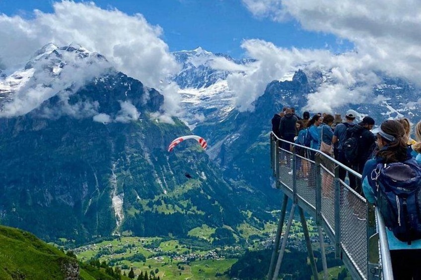 Un parapentista vuela sobre un paisaje montañoso mientras una multitud observa desde una plataforma. 1