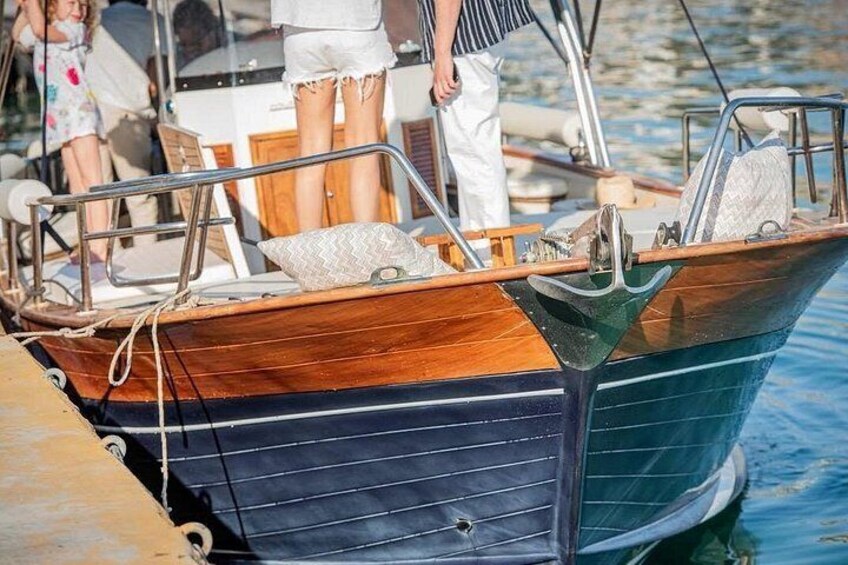 A wooden boat with a blue and green hull, docked at a pier with people around. 5