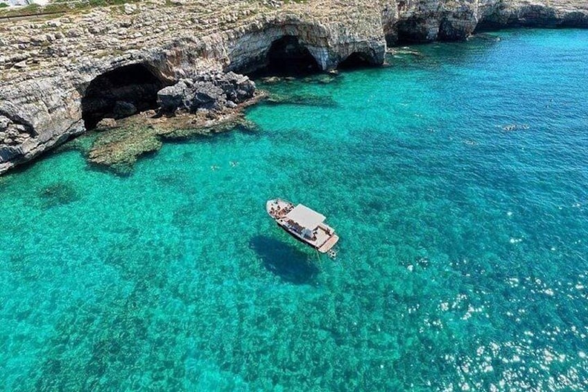 A boat in clear turquoise water near rocky cliffs. 1
