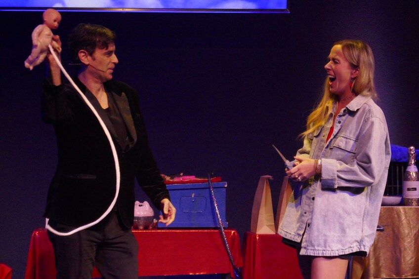 Two people on stage, one holding a microphone and the other holding a drink. 4