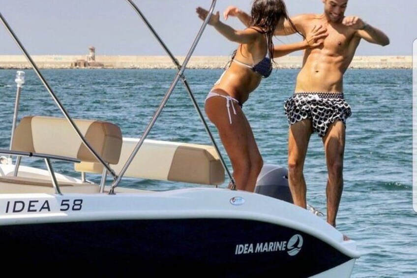 Un barco llamado IDEA 58 con dos personas de pie en la proa, cielo despejado y agua tranquila. 3
