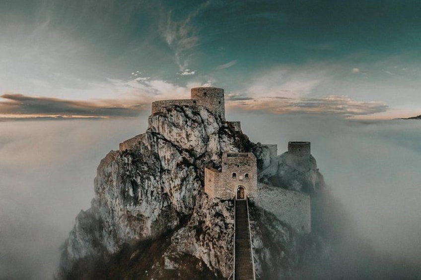 A castle perched on a cliff overlooking a misty valley. 1