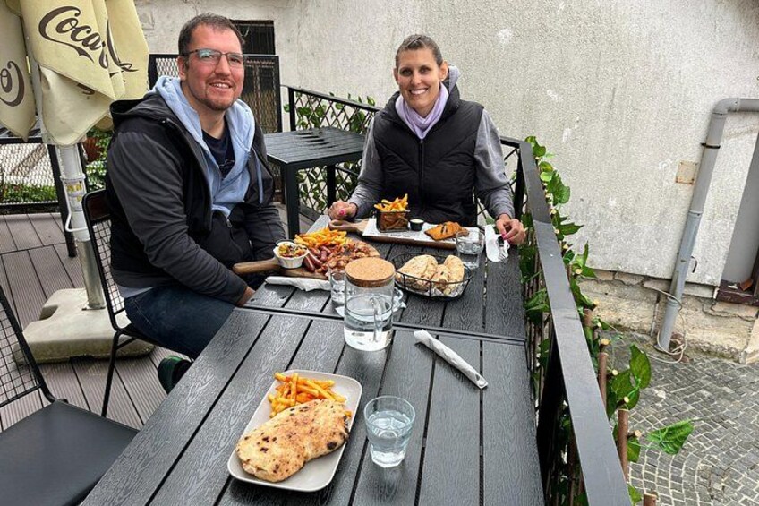 Zwei Personen essen und trinken an einem Tisch im Freien. 3