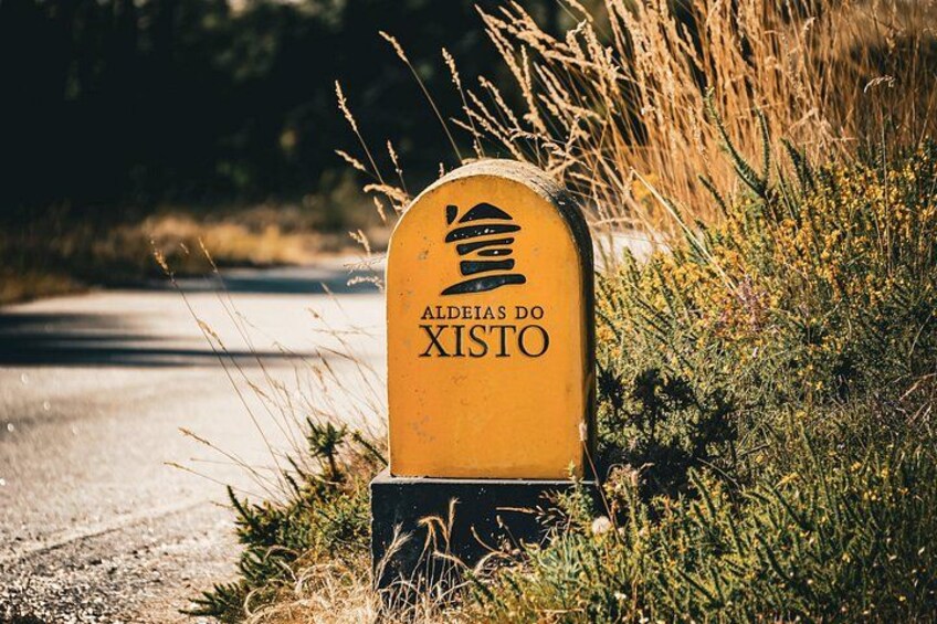 A yellow sign with the text 'ALDEIAS DO XISTO' in a rural setting. 3
