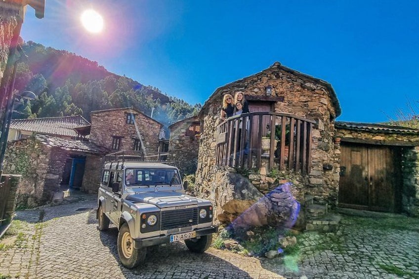 A stone building with a balcony, a parked vehicle, and a cobblestone path. 1