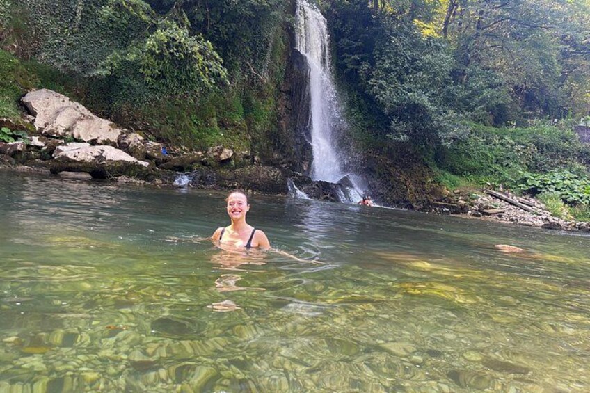 A person in clear water near a waterfall in a forested area. 4