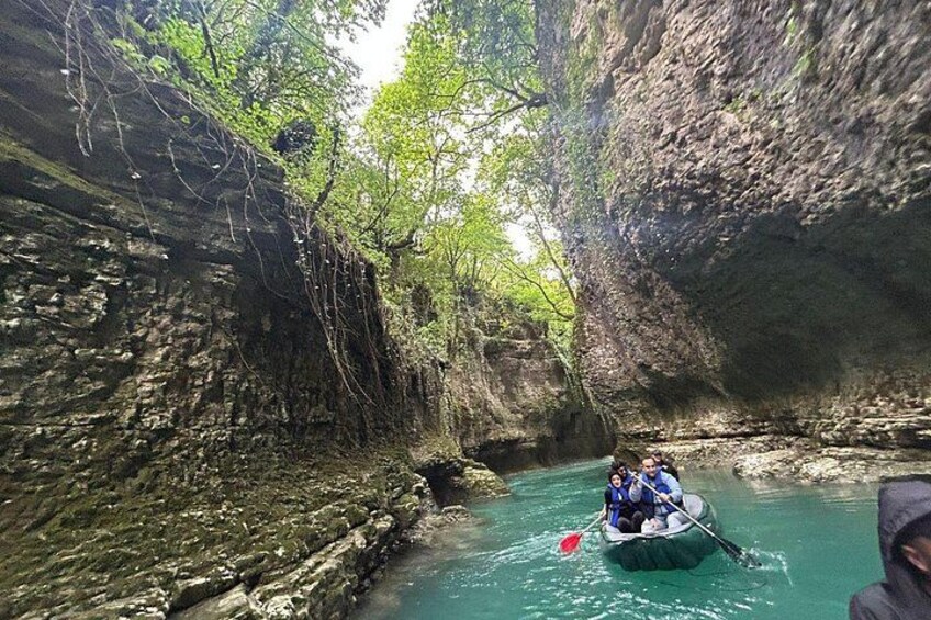 A narrow waterway with rocky walls, a boat with two people paddling, and lush greenery overhead. 5