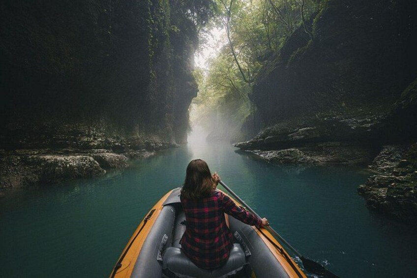 Eine Person sitzt in einem Kajak auf einem Fluss, umgeben von dichtem Wald. 1