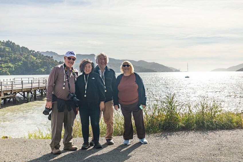 A group of people standing by a lake with a wooden dock and hills in the background. 1