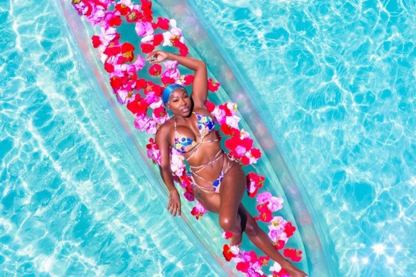 A person lying on a float in a pool surrounded by pink and red flowers. 4