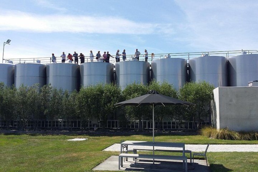 A group of people standing on large cylindrical tanks, a picnic table, and a grassy area with a fence. 2