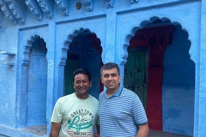 Two men standing in front of a blue building with arched doorways. 3