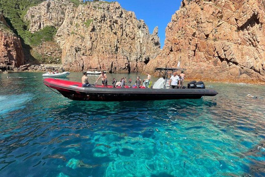 A boat with passengers on a clear blue sea, rocky cliffs in the background. 3
