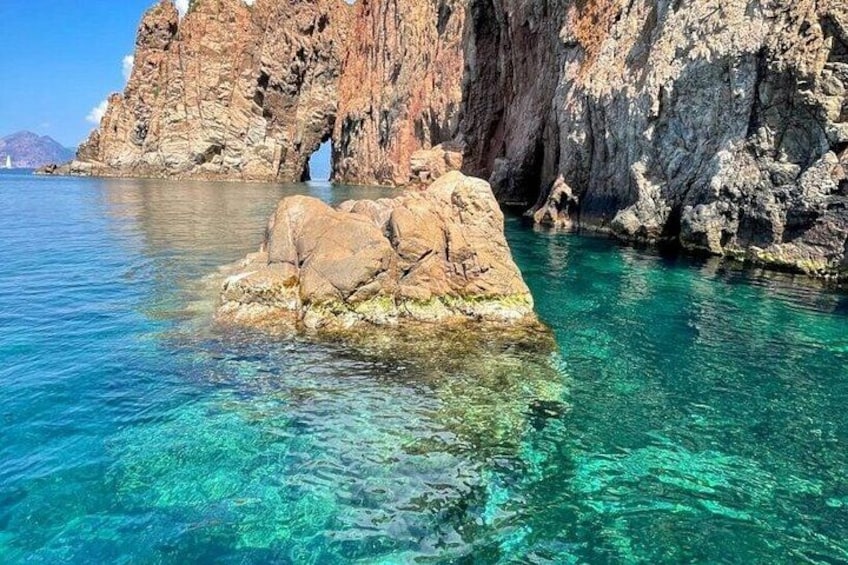 A rocky outcrop in clear blue water with a cave entrance. 5
