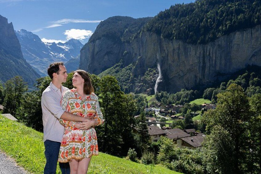 A couple embracing on a grassy hill with a mountainous landscape and a waterfall in the background. 1