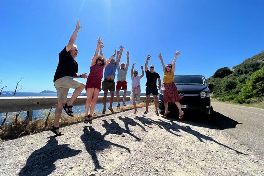 A group of people jumping in the air on a road with a car parked nearby. 3