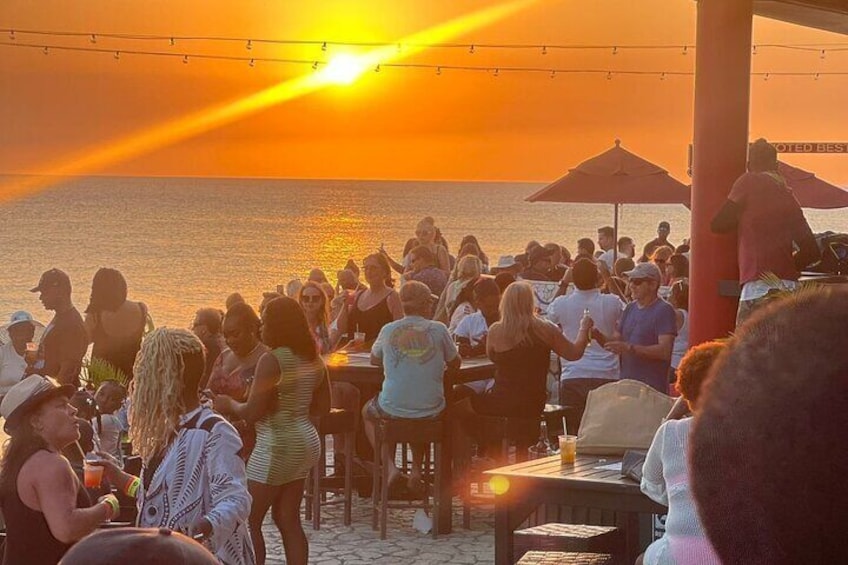 En grupp människor samlade på stranden vid solnedgången. 2