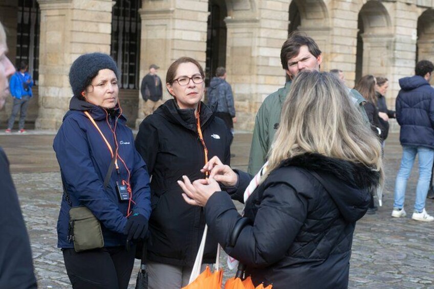 People standing and conversing in an outdoor area with stone buildings in the background. 2