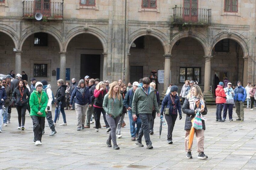 A crowded square with people walking, a historic building with arches, and a clear sky. 3