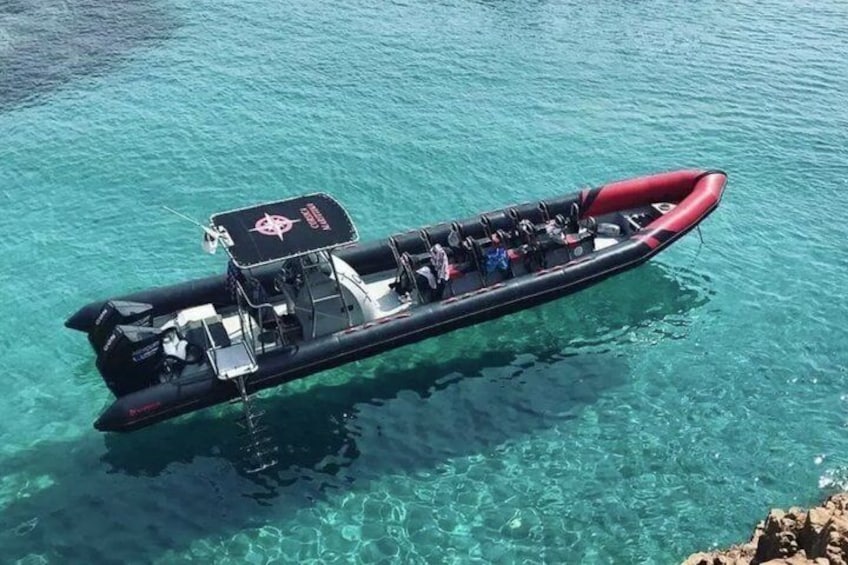 A long inflatable boat with passengers, floating on clear turquoise water. 2