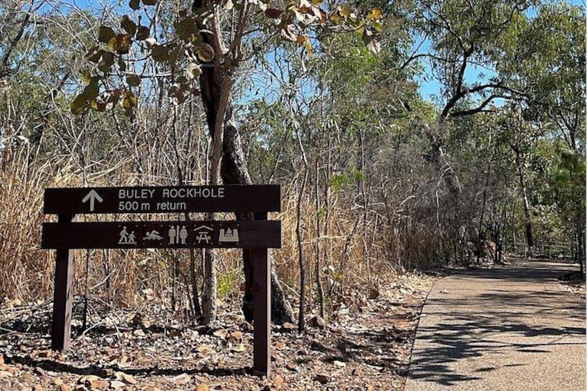 A signpost with directions to Buley Rockhole, 500m away, surrounded by dry trees and a dirt path. 3
