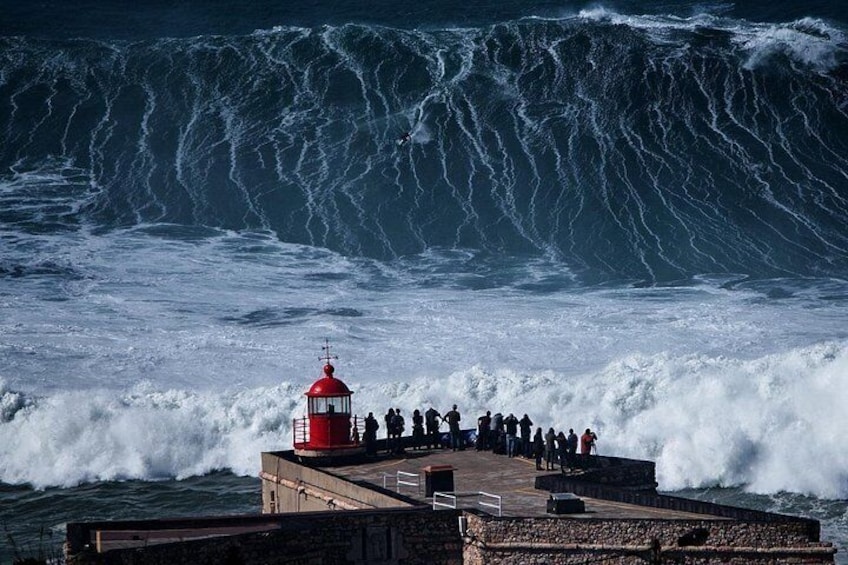 Un faro rojo, un muelle de piedra y una ola grande rompiendo sobre la orilla. 4