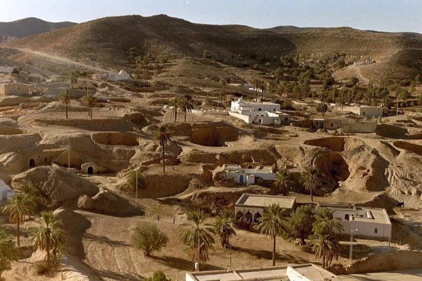 A desert landscape with scattered buildings, palm trees, and undulating terrain. 5