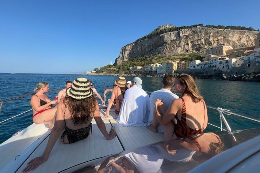 A group of people on a boat near a coastal town with buildings on a cliff. 4
