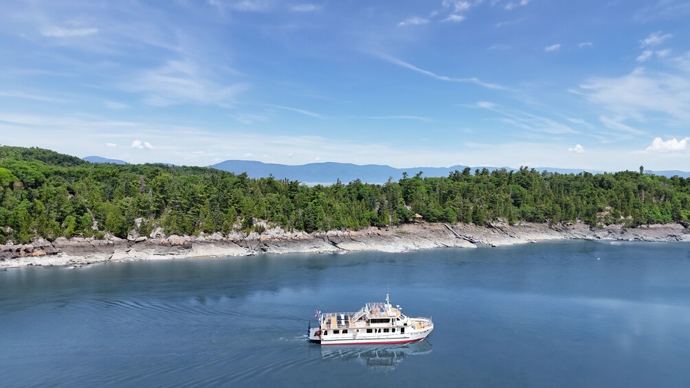 A white boat with red trim on calm water, surrounded by a forested shoreline and distant mountains. 2