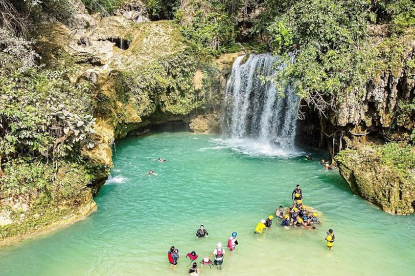 A waterfall, clear turquoise water, and people swimming and floating. 4