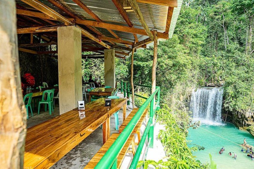 A wooden deck with green chairs overlooking a waterfall and a turquoise pool. 2