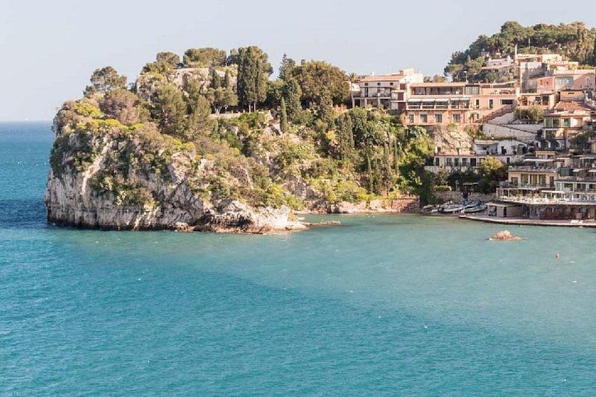 Un pueblo costero con edificios en un acantilado, mar azul cristalino y un promontorio rocoso. 4