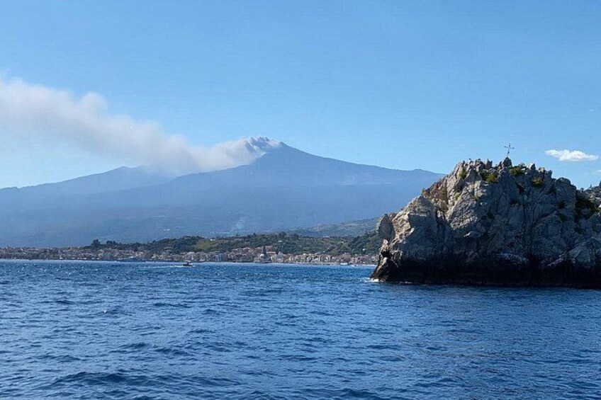 Paesaggio costiero con una montagna sullo sfondo, un promontorio roccioso con vegetazione e mare calmo. 3