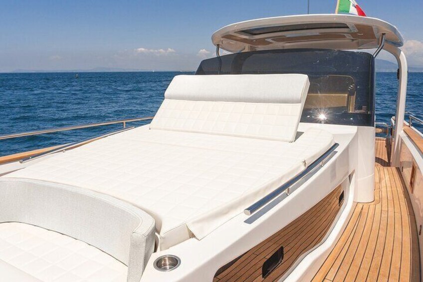 A boat deck with a white cushioned area, wooden flooring, and a view of the sea. 4