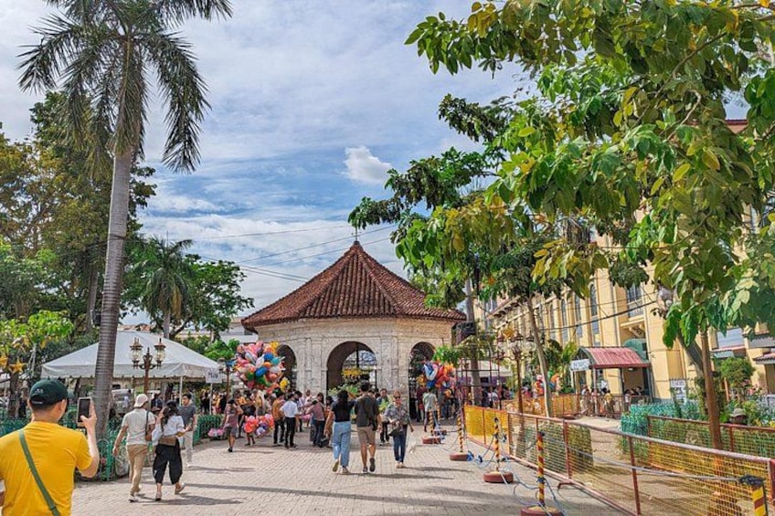A bustling outdoor plaza with a traditional building, palm trees, and a crowd of people. 4