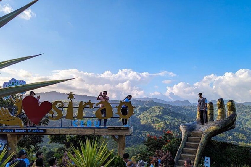 A sign with 'Sira' and 'Cerro' on a wooden platform with a view of mountains. 1
