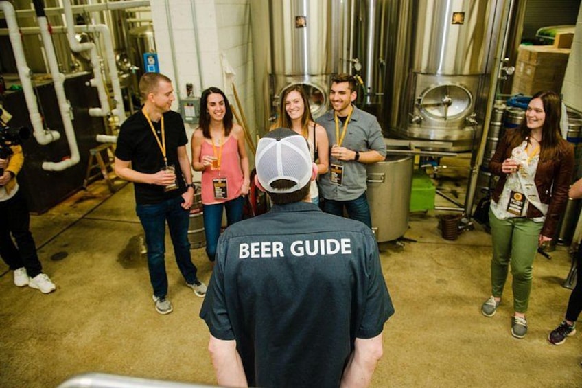 Un gruppo di persone in un birrificio, tra cui una persona con una maglietta con scritto 'BEER GUIDE'. 3