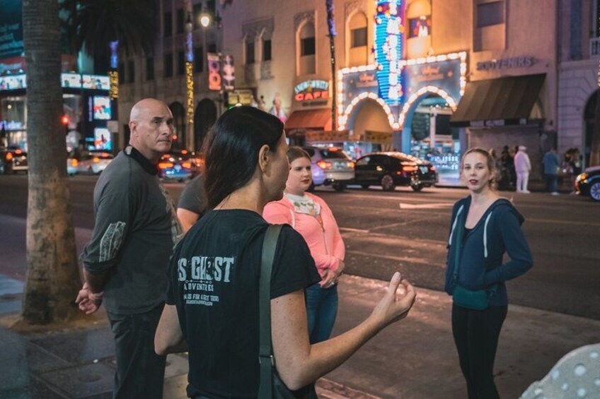 A group of people standing on a sidewalk at night with illuminated buildings in the background. 4