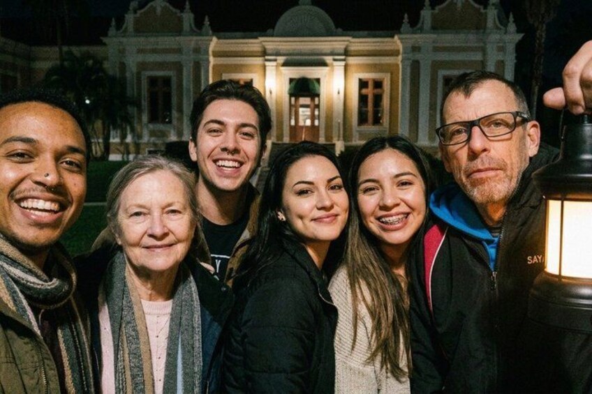 A group of people posing in front of a historic building at night. 3