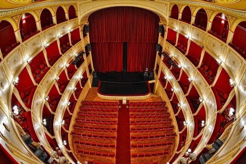 A grand theater with a red stage, ornate golden balconies, and rows of red seats. 3