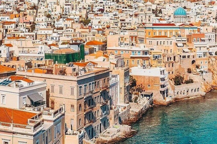 A coastal cityscape with densely packed buildings, a prominent dome structure, and a clear blue waterfront. 2