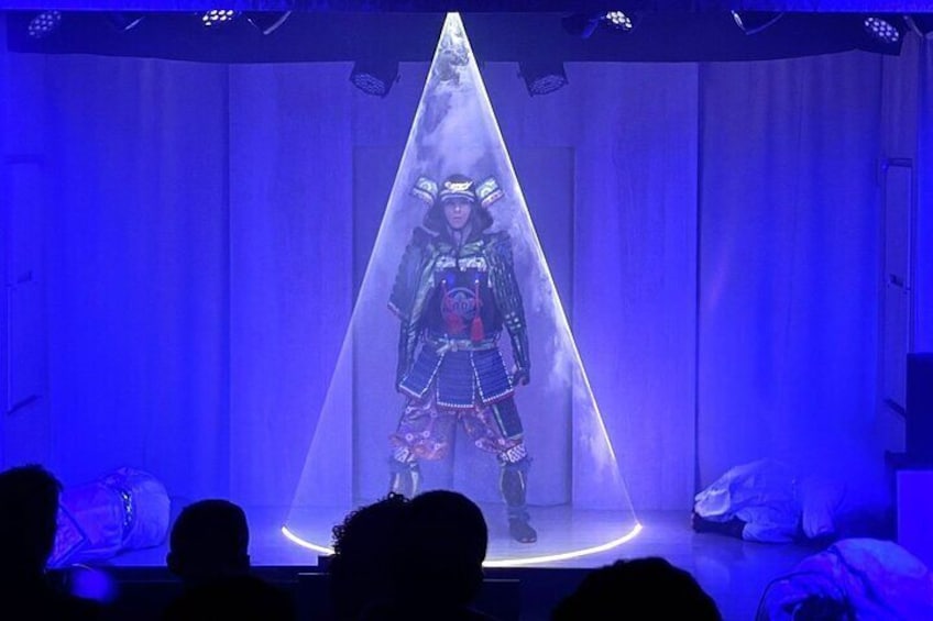 Una persona vestida con traje tradicional de pie bajo un foco en un escenario. 5