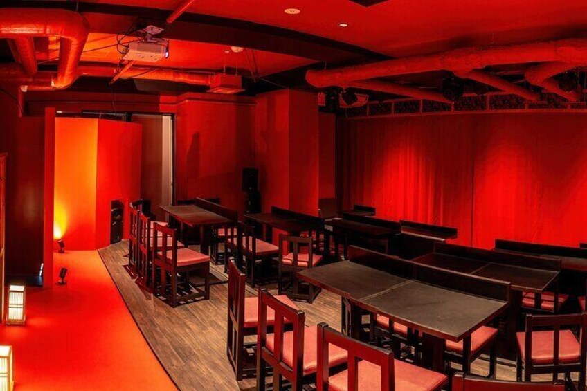 Una habitación iluminada en rojo con mesas, sillas, un escenario y un proyector. 4
