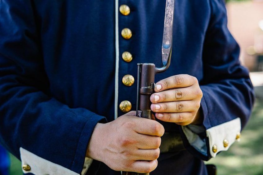 A person holding a rifle with a bayonet attached, wearing a dark blue uniform with gold buttons. 3