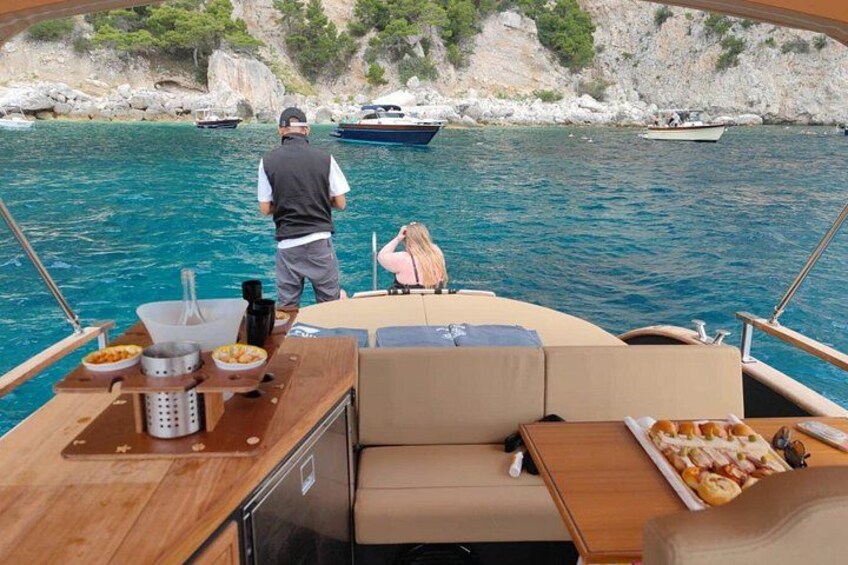 A boat with a wooden deck, a person standing at the bow, and another person seated. 4