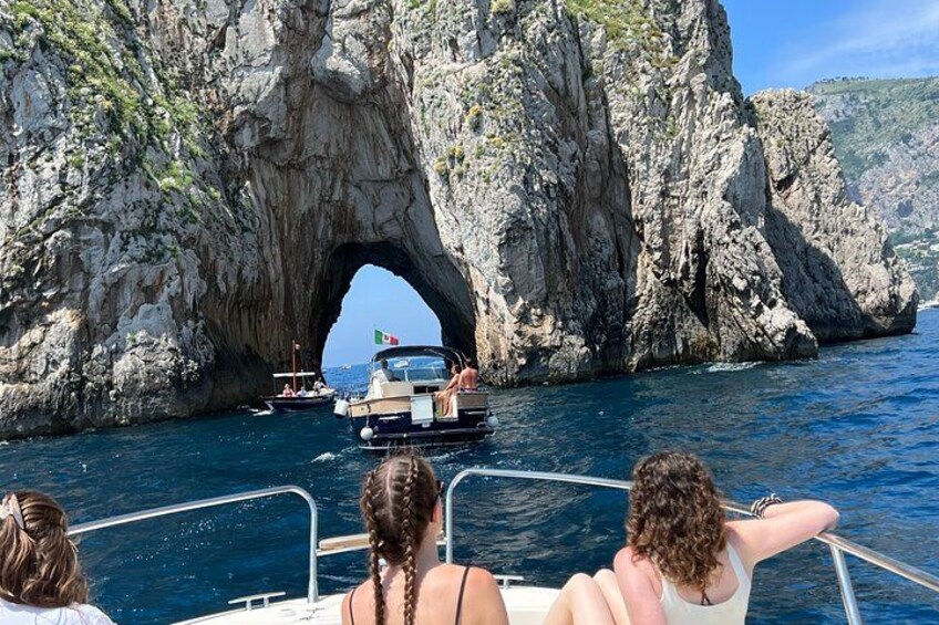 A boat passing through a natural rock arch in a body of water. 3